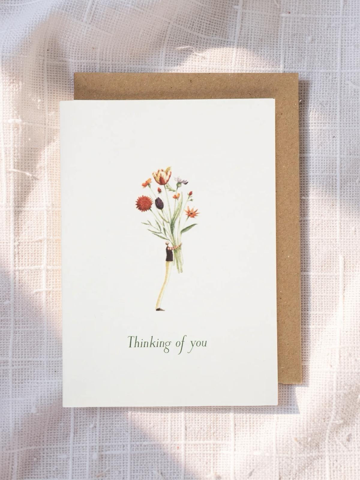 Greeting card with floral illustration and 'Thinking of you' text on a textured fabric background.