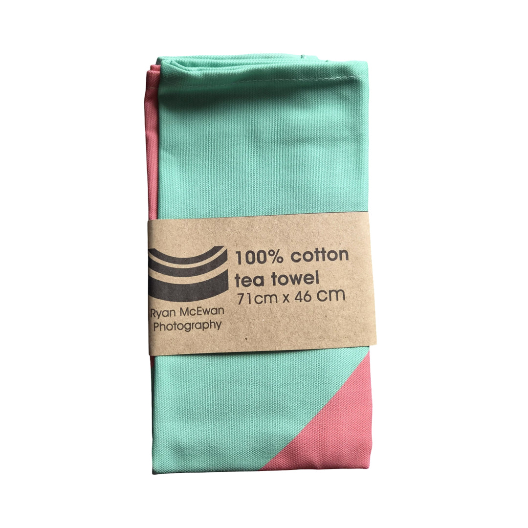 Folded teal and pink tea towel with a brown label on a white background