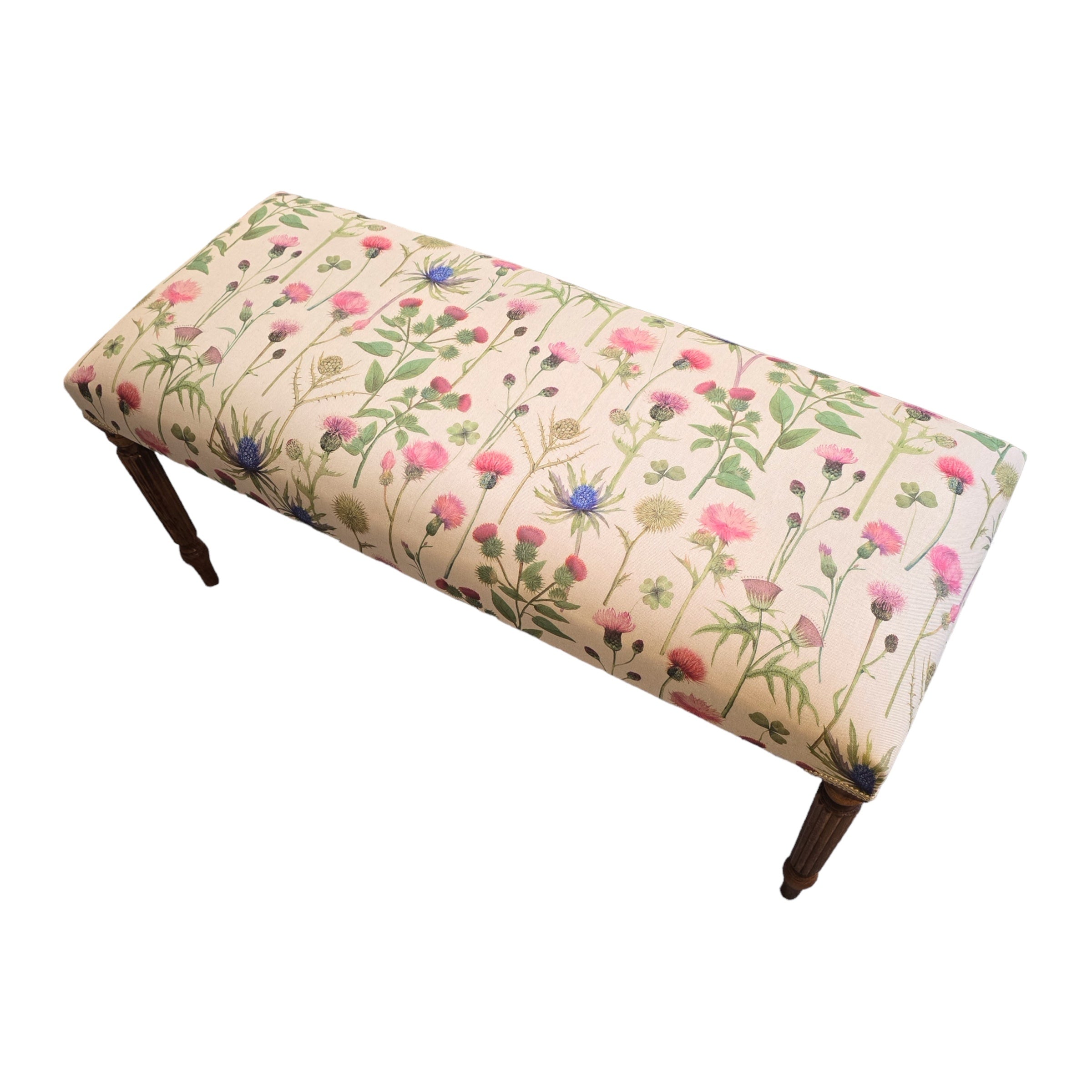 A rectangular bench with cream linen upholstery, featuring a floral pattern with pink and purple thistles and green foliage, and mahogany legs.