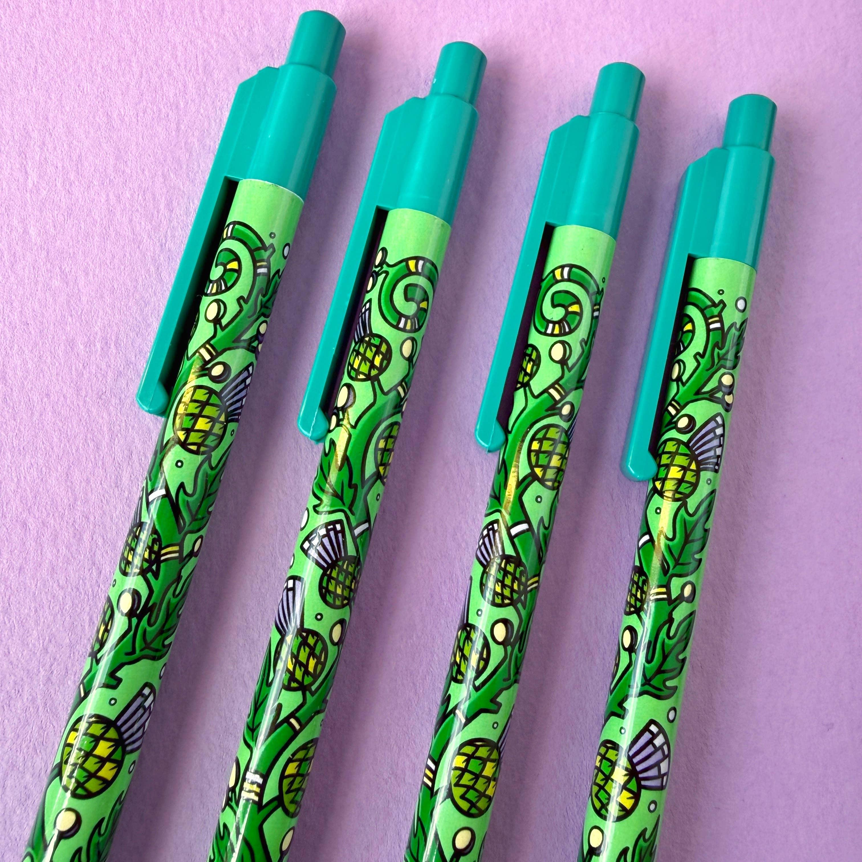 Four green pens with thistle design on a purple background.
