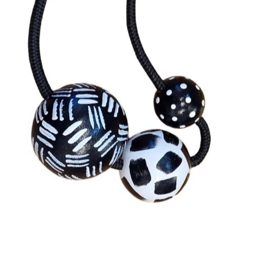 A black and white chunky necklace with three beads featuring dashes, strokes, and polka dot patterns, strung on black braided soutache rope, with an adjustable length.