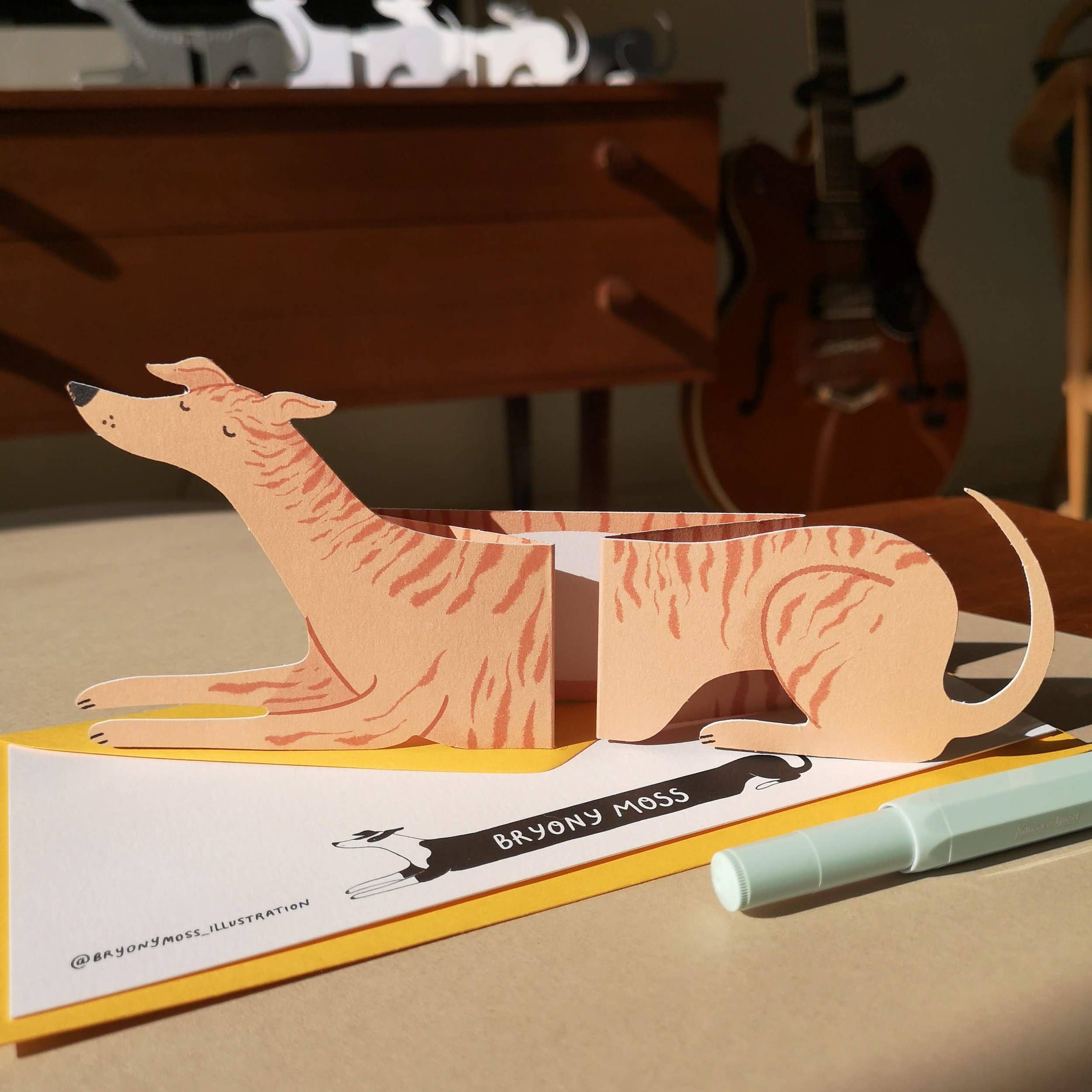 Card with a dog illustration on a table with a pen and guitar in the background.