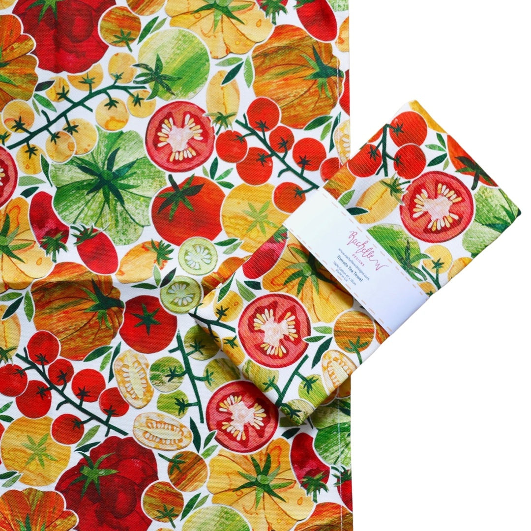 Tea towel featuring red, orange and yellow tomatoes with green foliage on a white background.