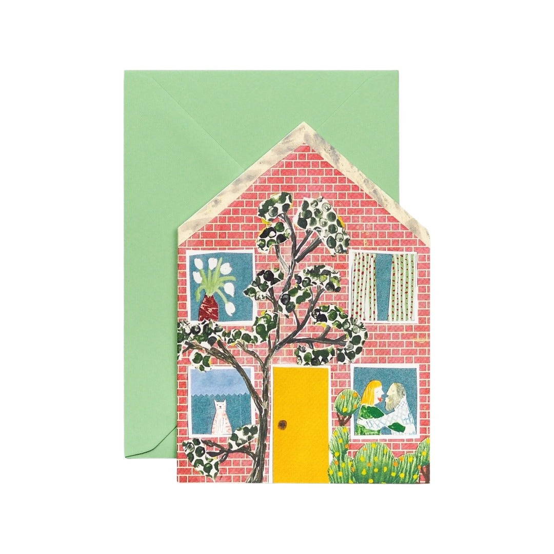 A  card featuring an illustration of a brick house with a gorgeous yellow door and tree growing outside, and a pale green envelope