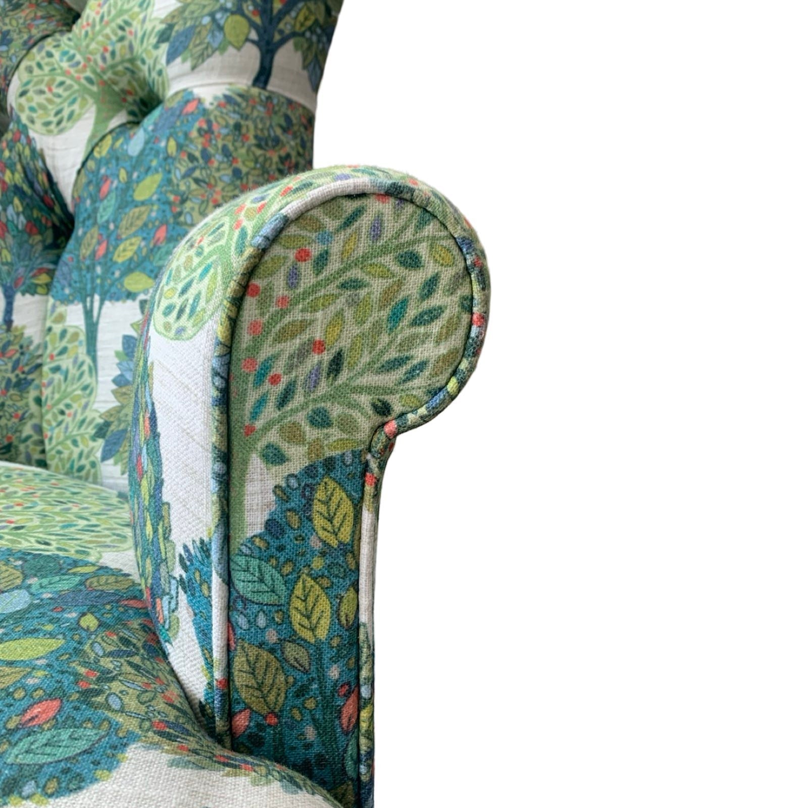 A cream linen armchair with a blue and green tree pattern, featuring a button-back design, mahogany legs, and gold castors.