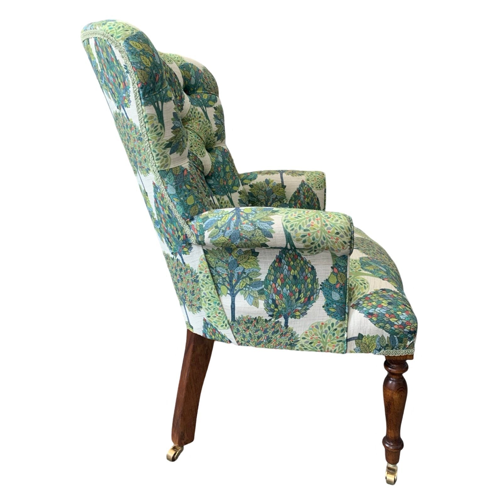 A cream linen armchair with a blue and green tree pattern, featuring a button-back design, mahogany legs, and gold castors.