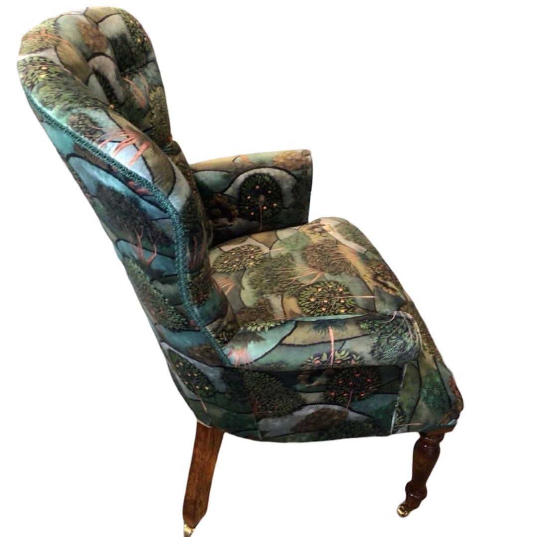 A green velvet armchair with a pattern of trees and hills, featuring a button-back design and mahogany legs.