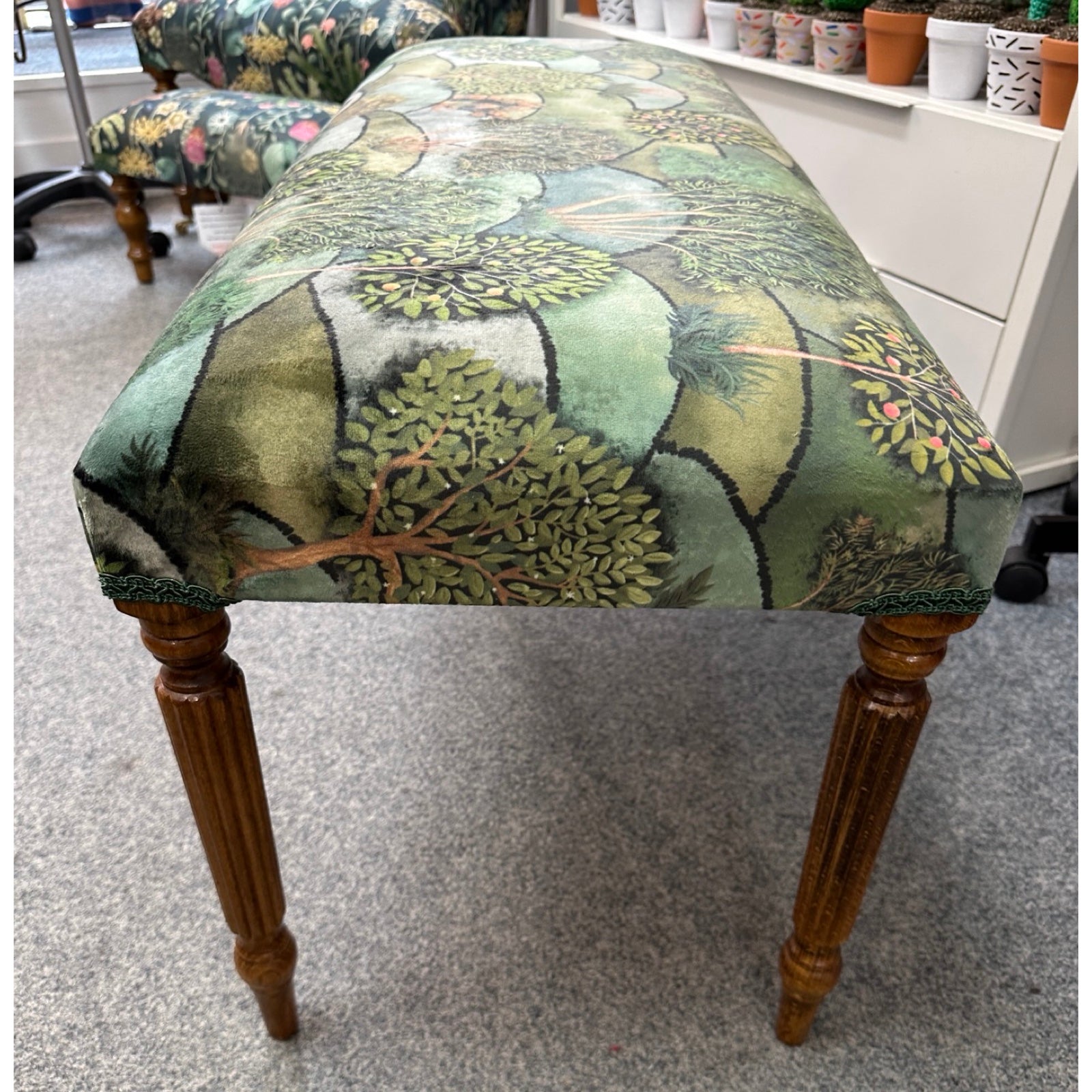Wooden stool with a green leaf-patterned fabric cover in an indoor setting.