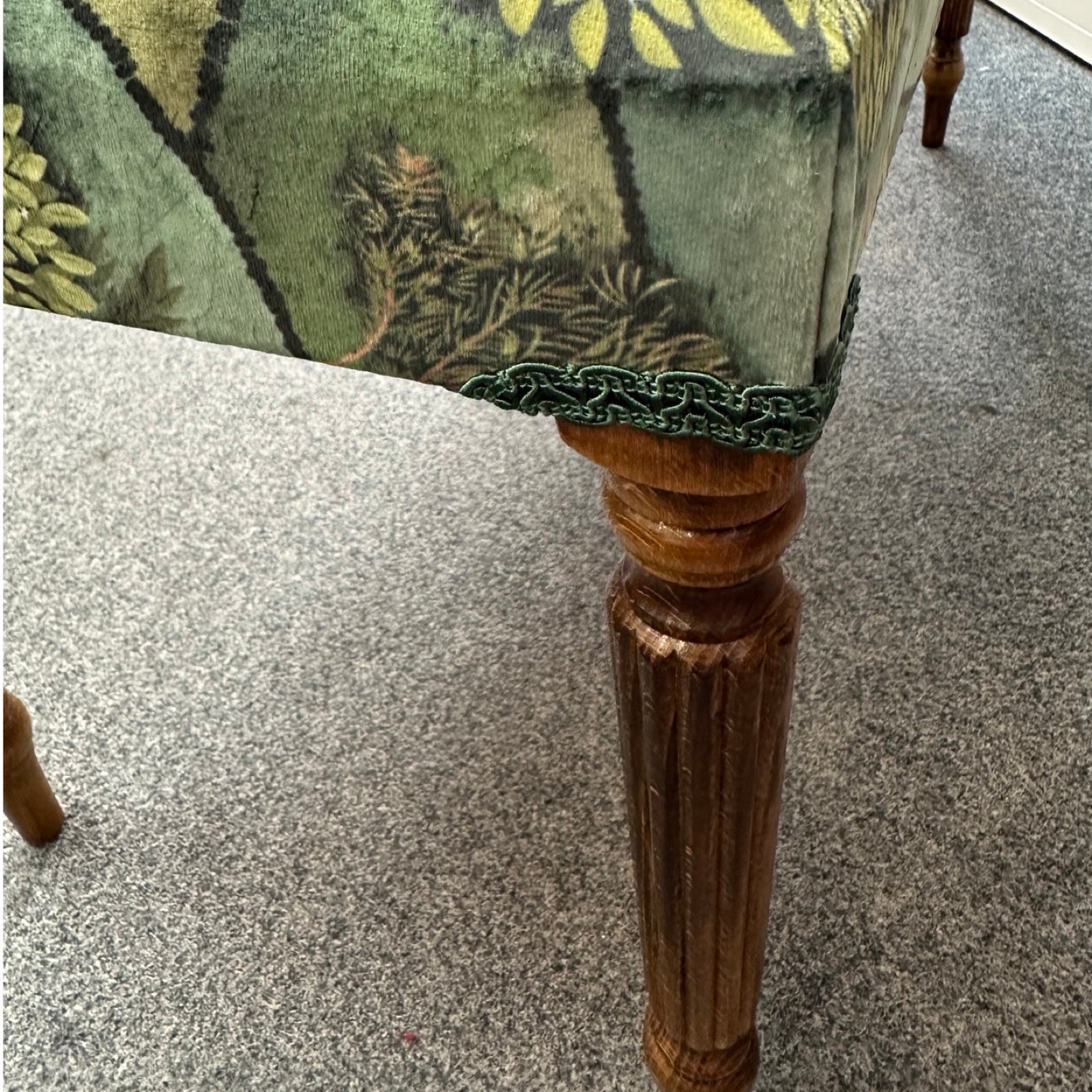 Close-up of a wooden leg with floral-patterned fabric on a carpeted floor.