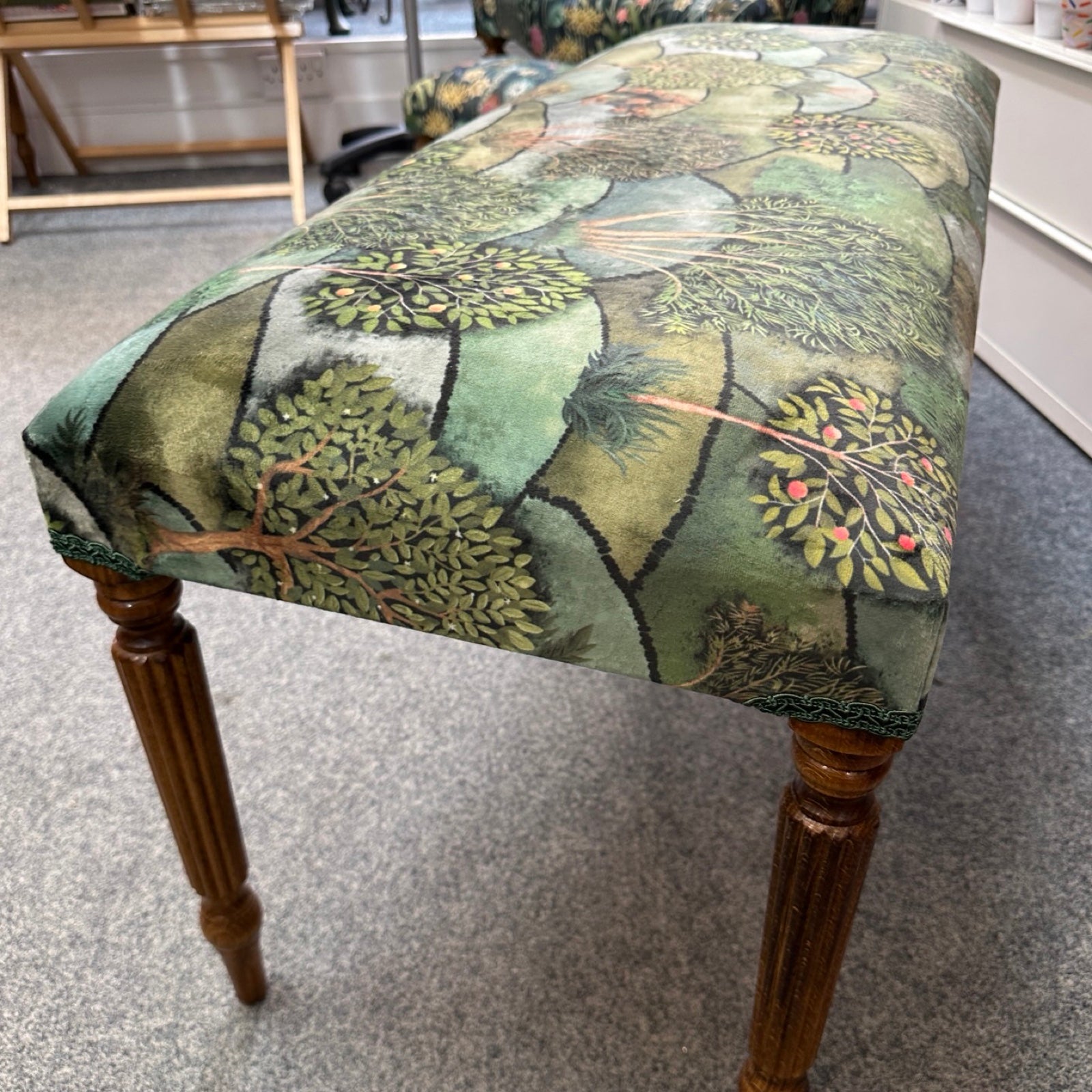 Fabric-covered bench with nature-themed design on a gray floor.