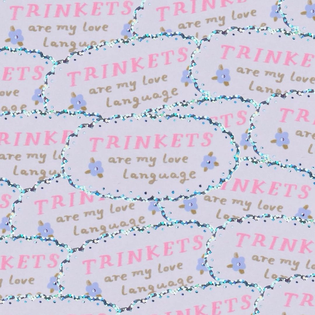 A close-up of a pile of stickers with a glittery boarder, and text reading 'trinkets are my love language'.