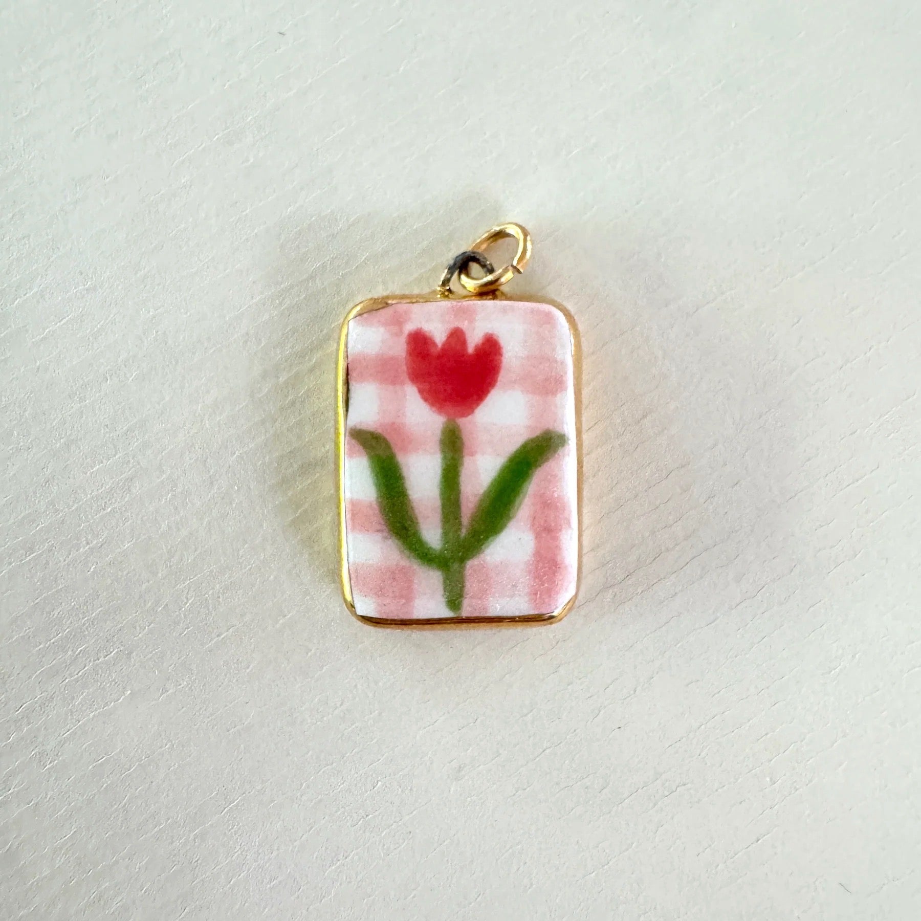 Small rectangular pendant with a red tulip design on a pink checkered background, set against a light grey background.