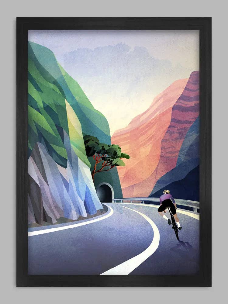 Framed artwork of a cyclist on a winding road with colourful mountains.