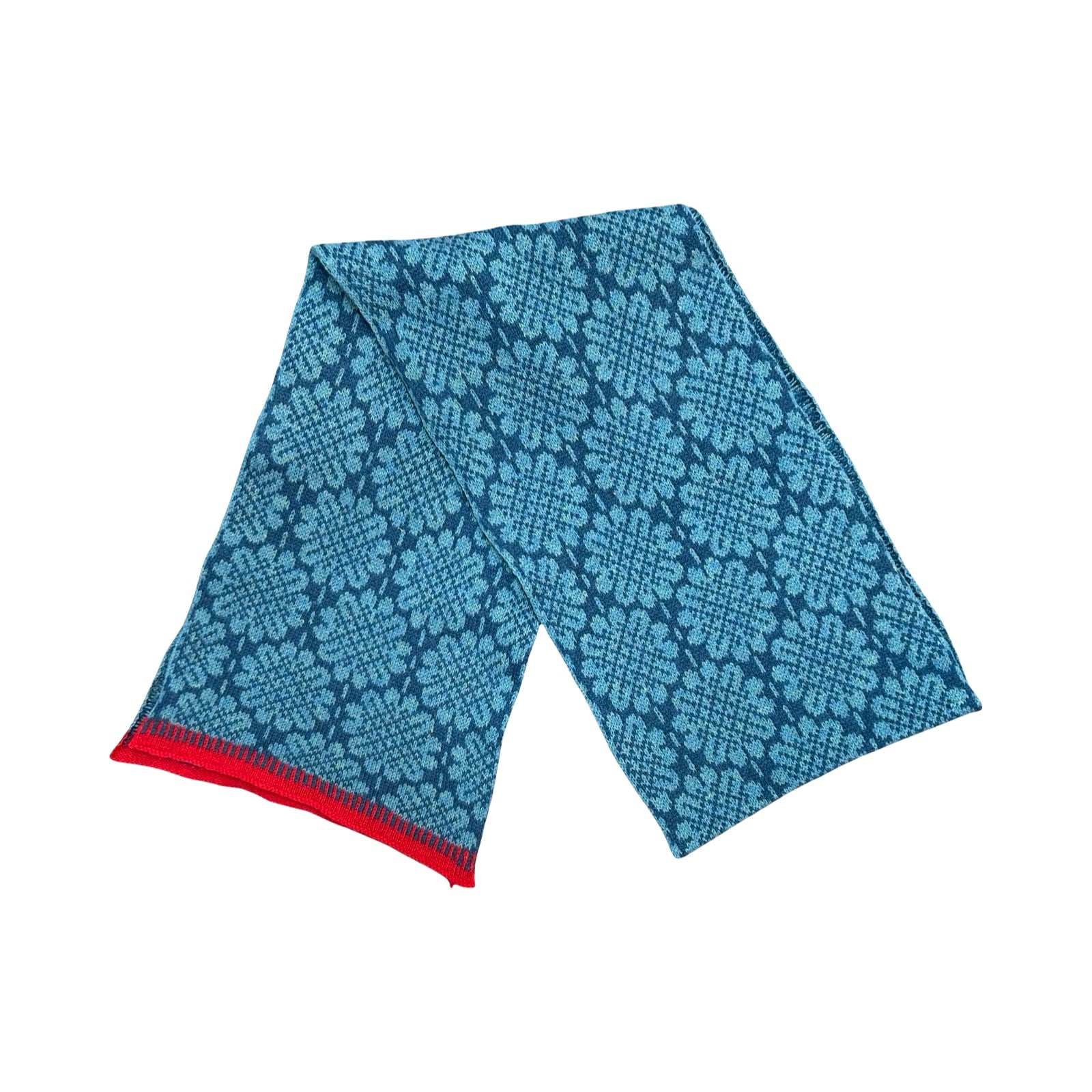 A 100% lambswool knitted scarf with a turquoise daisy pattern against a blue background with contrasting red edges.