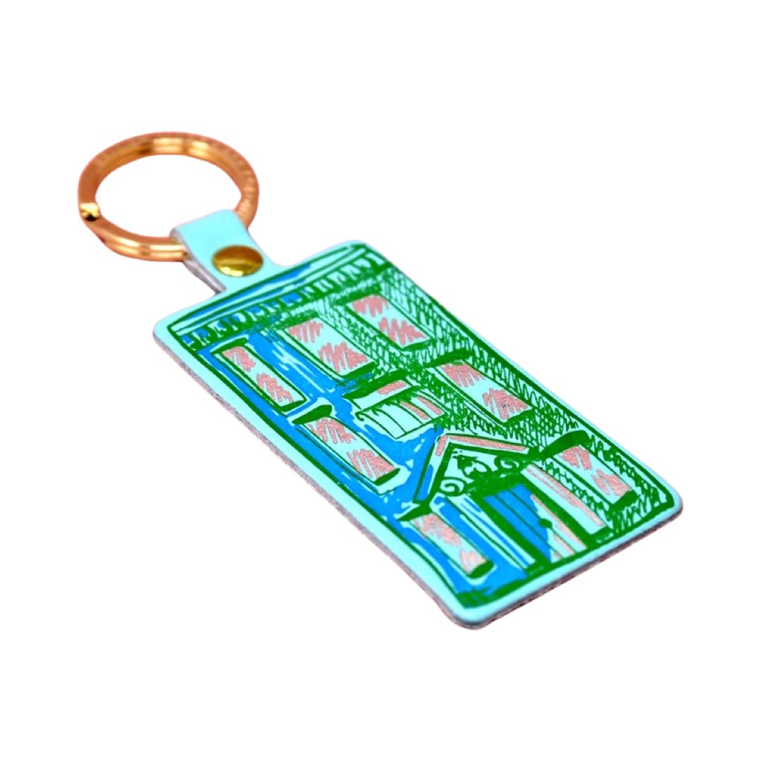 A turquoise rectangular leather keyring with an illustration of an apartment block in green and a gold-coloured keyring. 