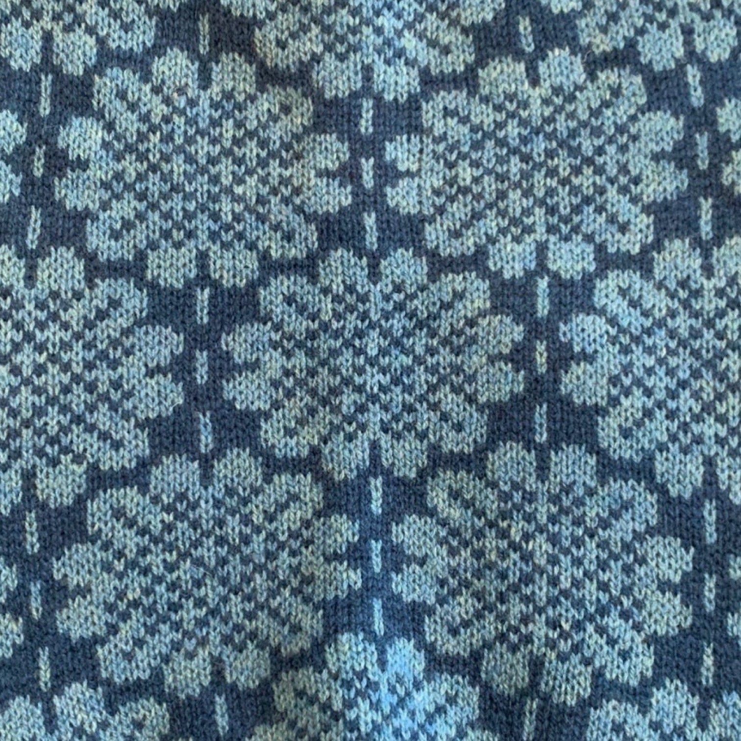 A soft and cosy 100% lambswool knitted snood in a turquoise daisy design against a blue background.