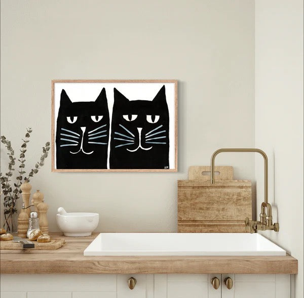 This art print features the heads of two black cats against a white background, above a kitchen sink.