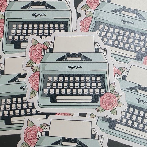 A sticker featuring an illustration of a turquoise typewriter surrounded by three pink roses.