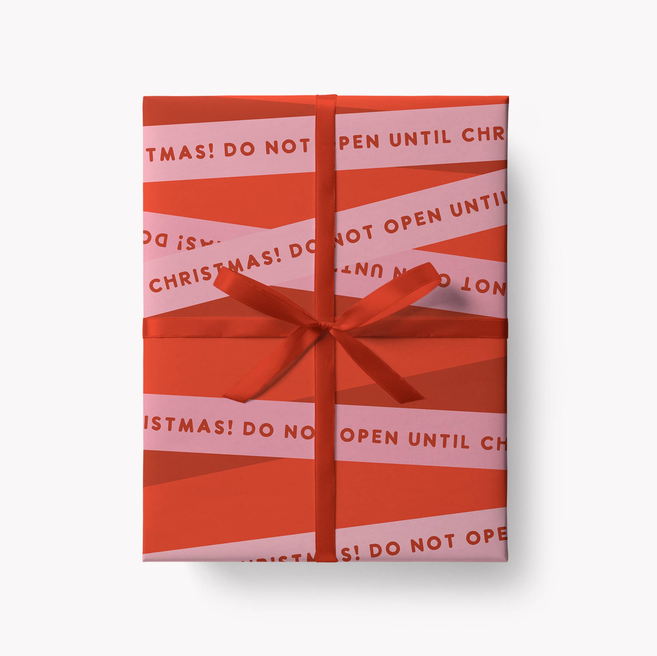 A rectangular gift box wrapped in red and light pink striped paper with 'DO NOT OPEN UNTIL CHRISTMAS!' printed repeatedly, tied with a matching red ribbon and bow, on a light grey background.