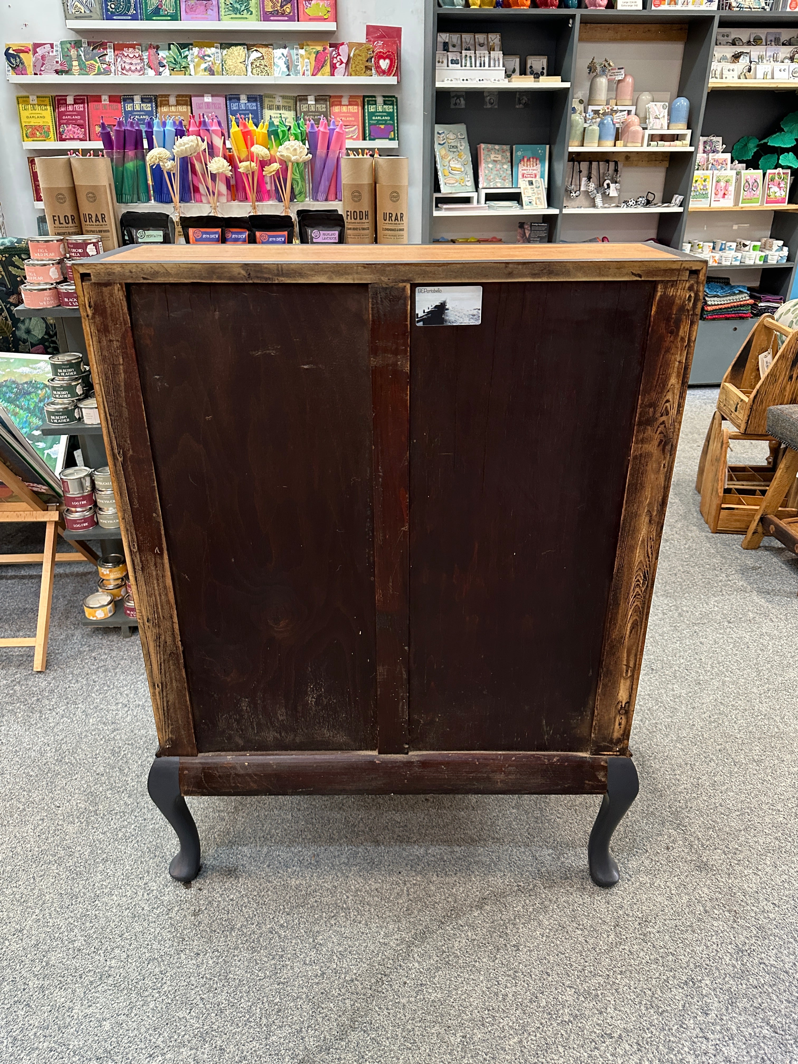 Wooden bureau with a dark finish on a store floor with shelves and products.
