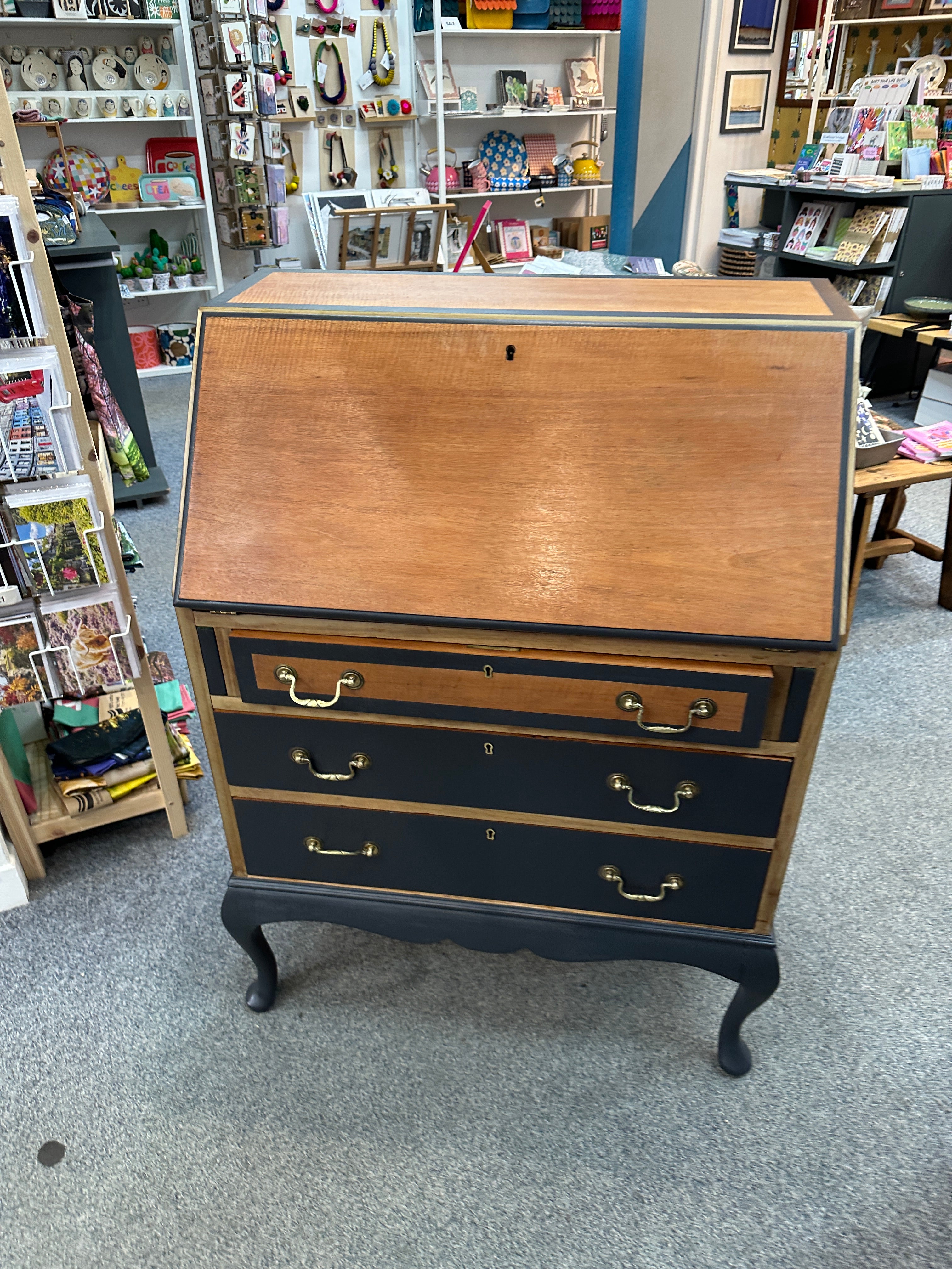 Wooden dresser with black accents and gold handles in a store setting.