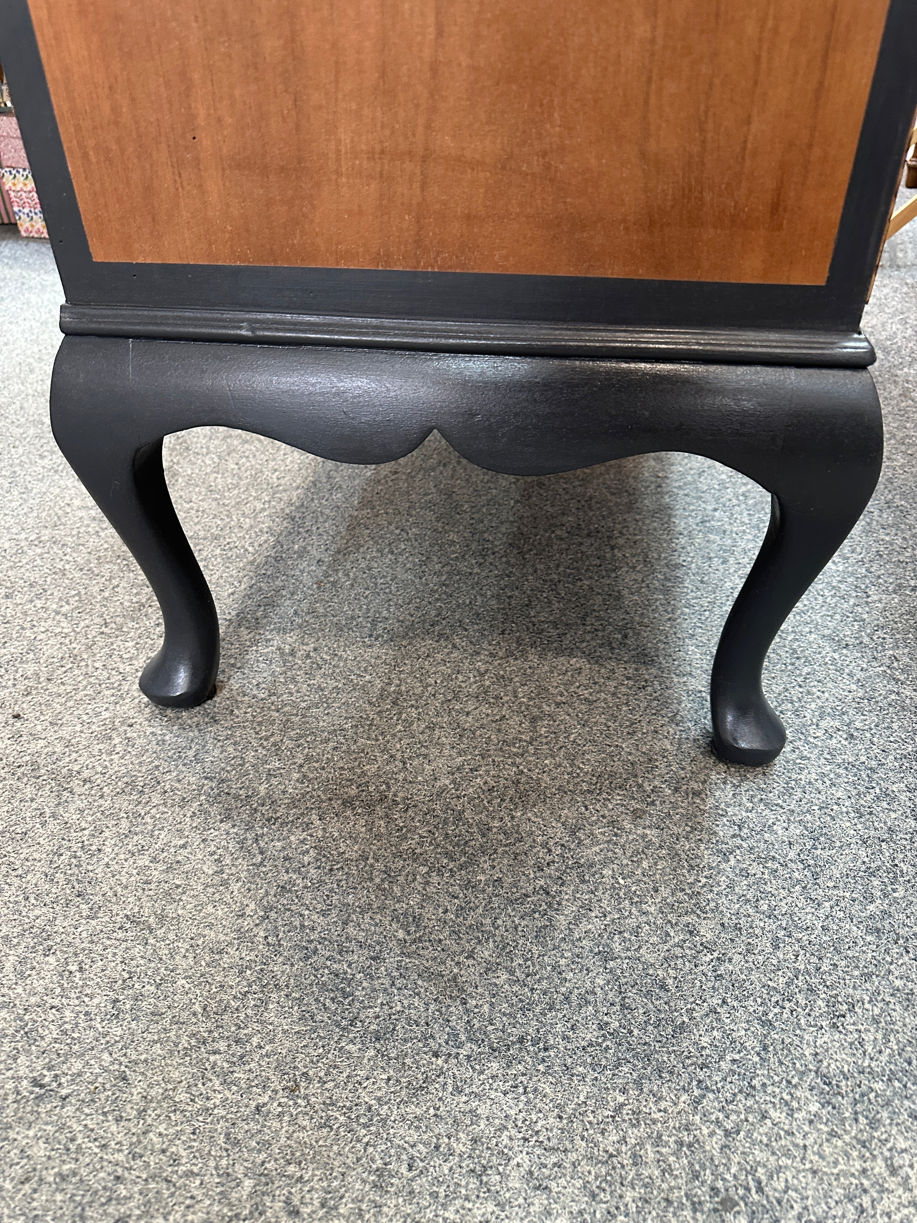 Wooden side table with black legs on a grey carpet.