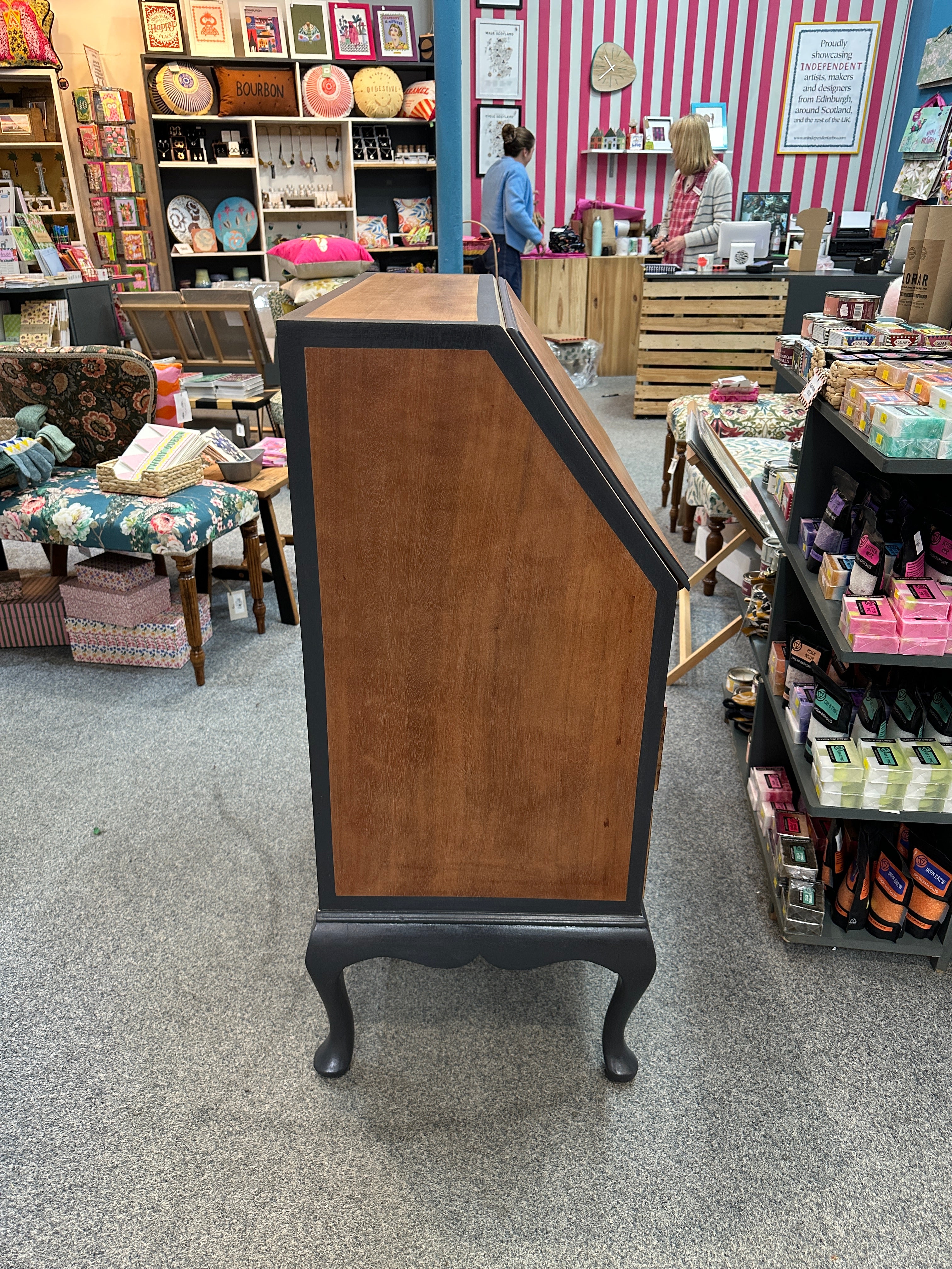 Wooden bureau with a brown side and black legs in a store setting.
