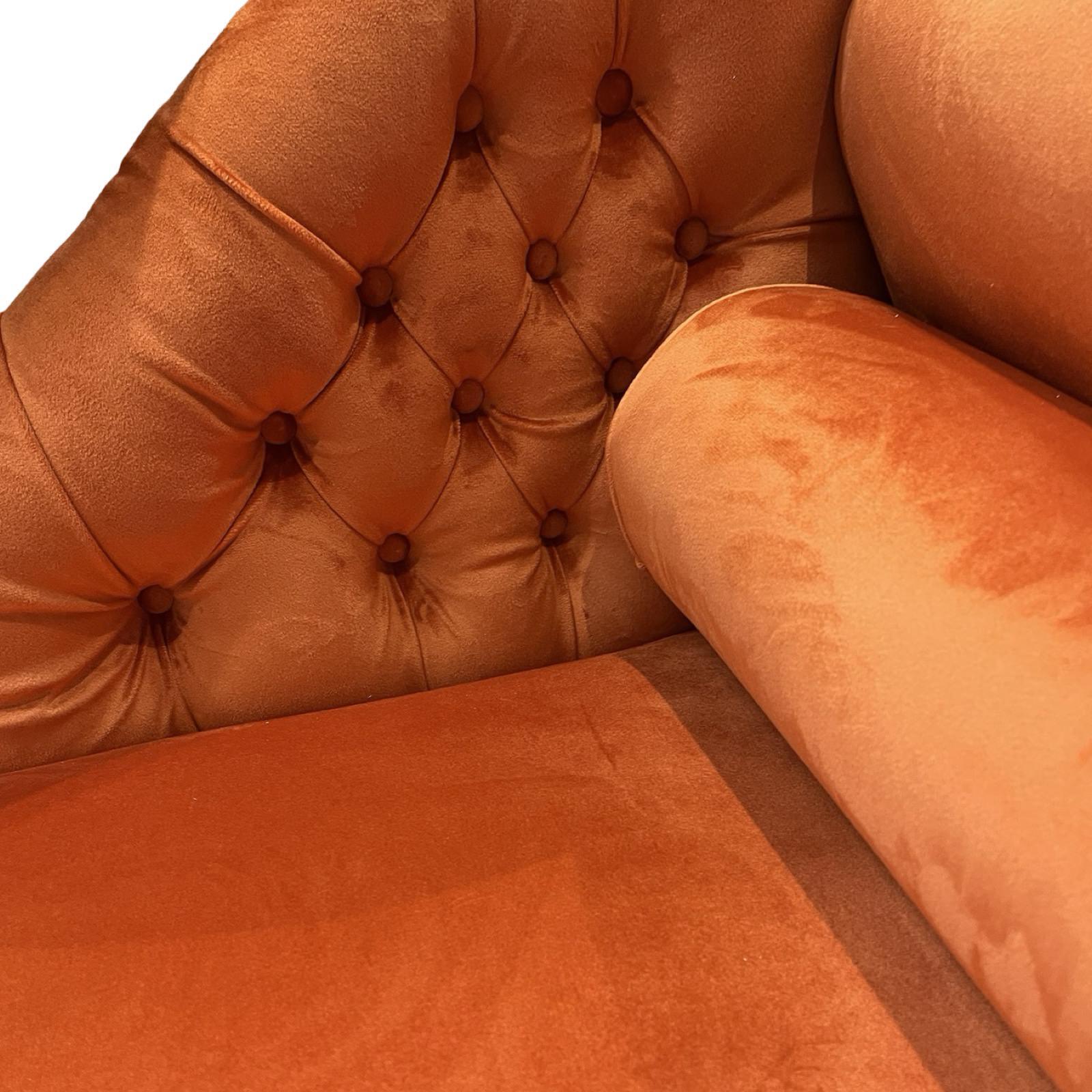 An orange velvet chaise longue with mahogany stained legs and brass coloured castors.