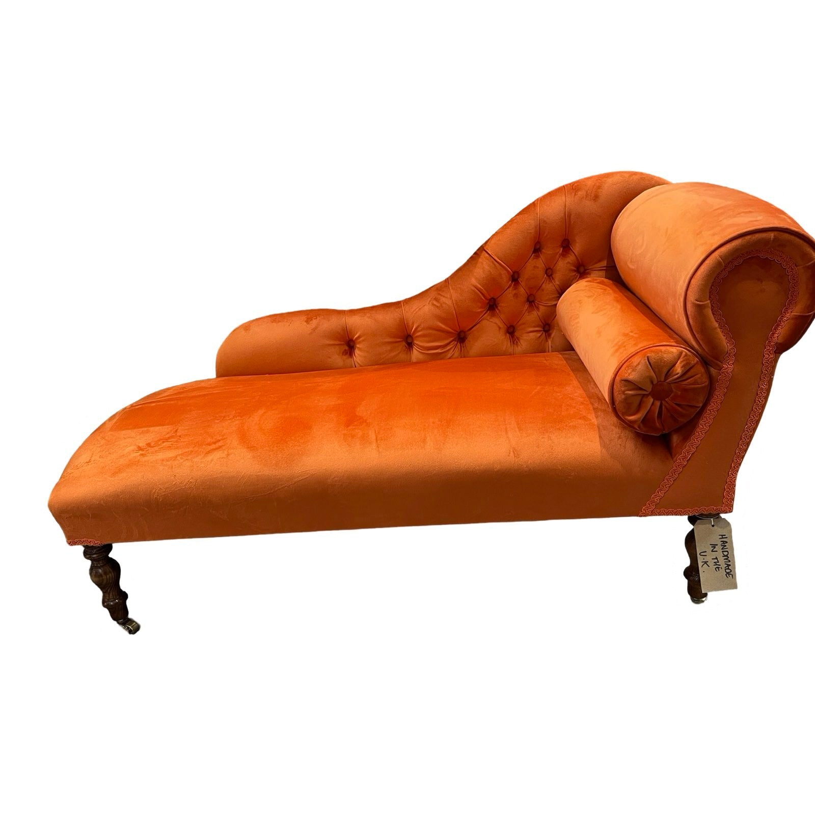An orange velvet chaise longue with mahogany stained legs and brass coloured castors.