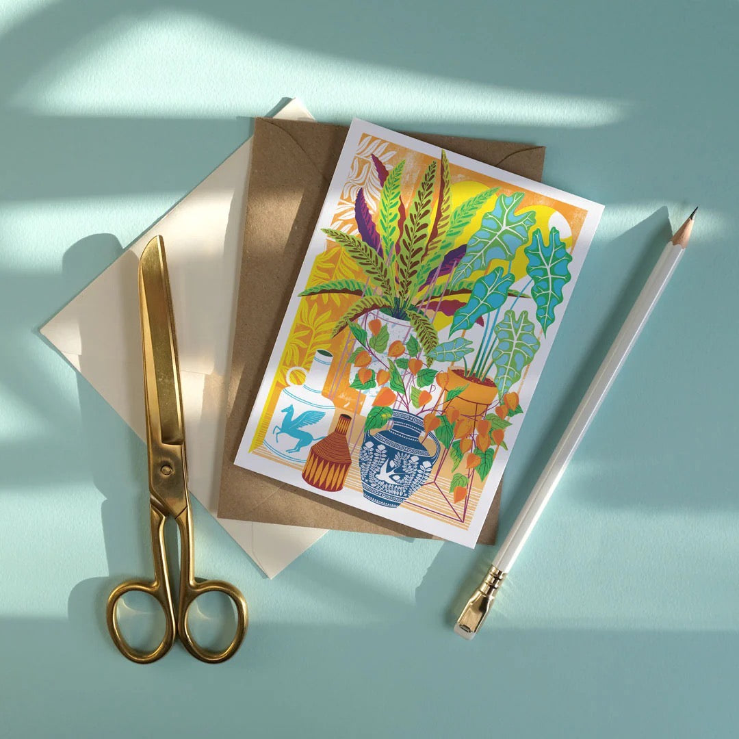Greeting card with plant illustration, envelope, scissors, and pen on a light blue background.