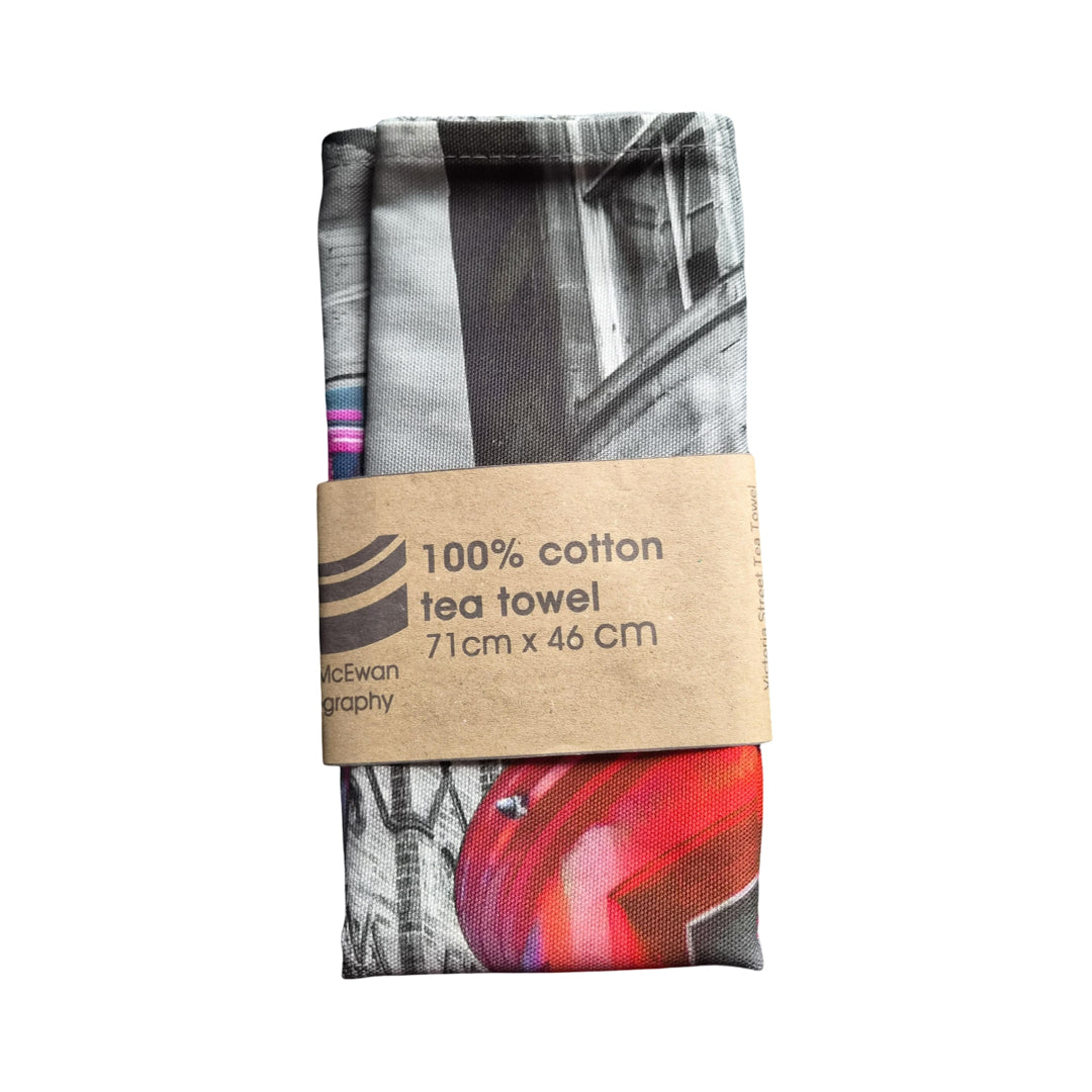 Tea towel with a black and white design and a red accent, wrapped in brown paper with text.