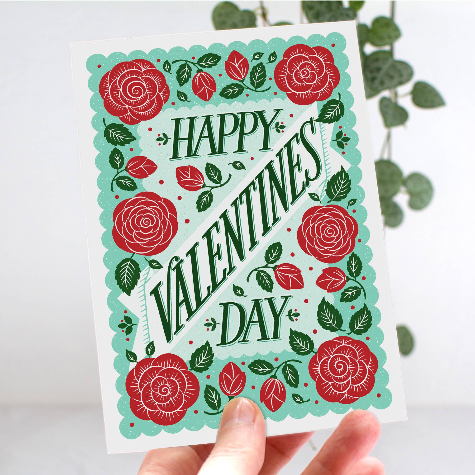 Valentine's Day card with red roses and green leaves held by a hand against a light background.