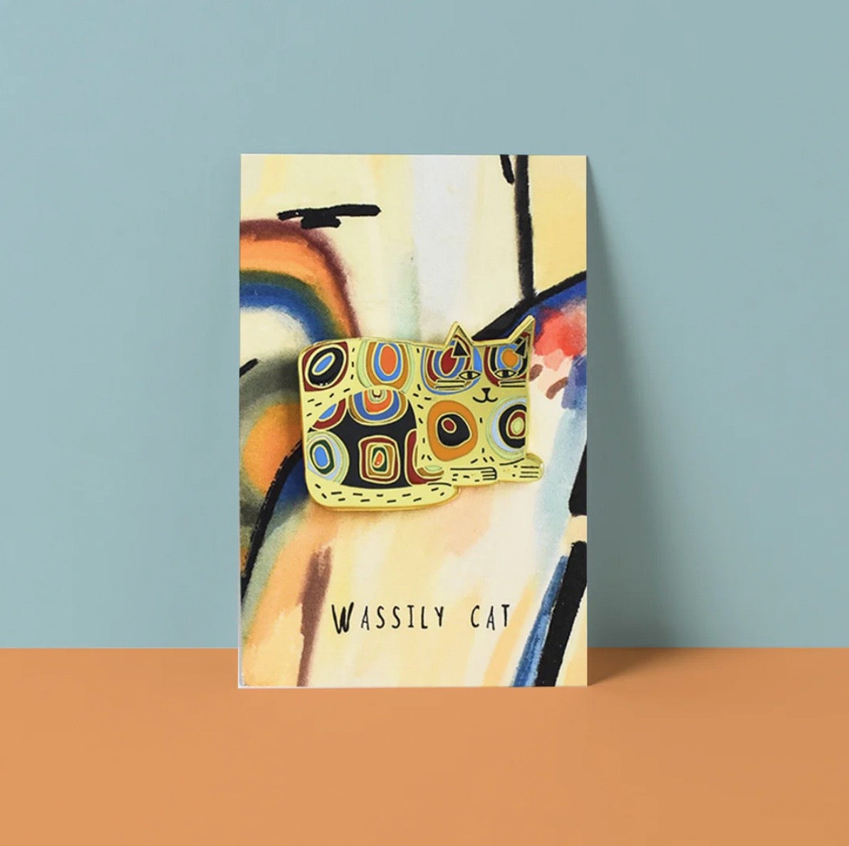 Colourful cat-shaped pin on backing card with abstract design.