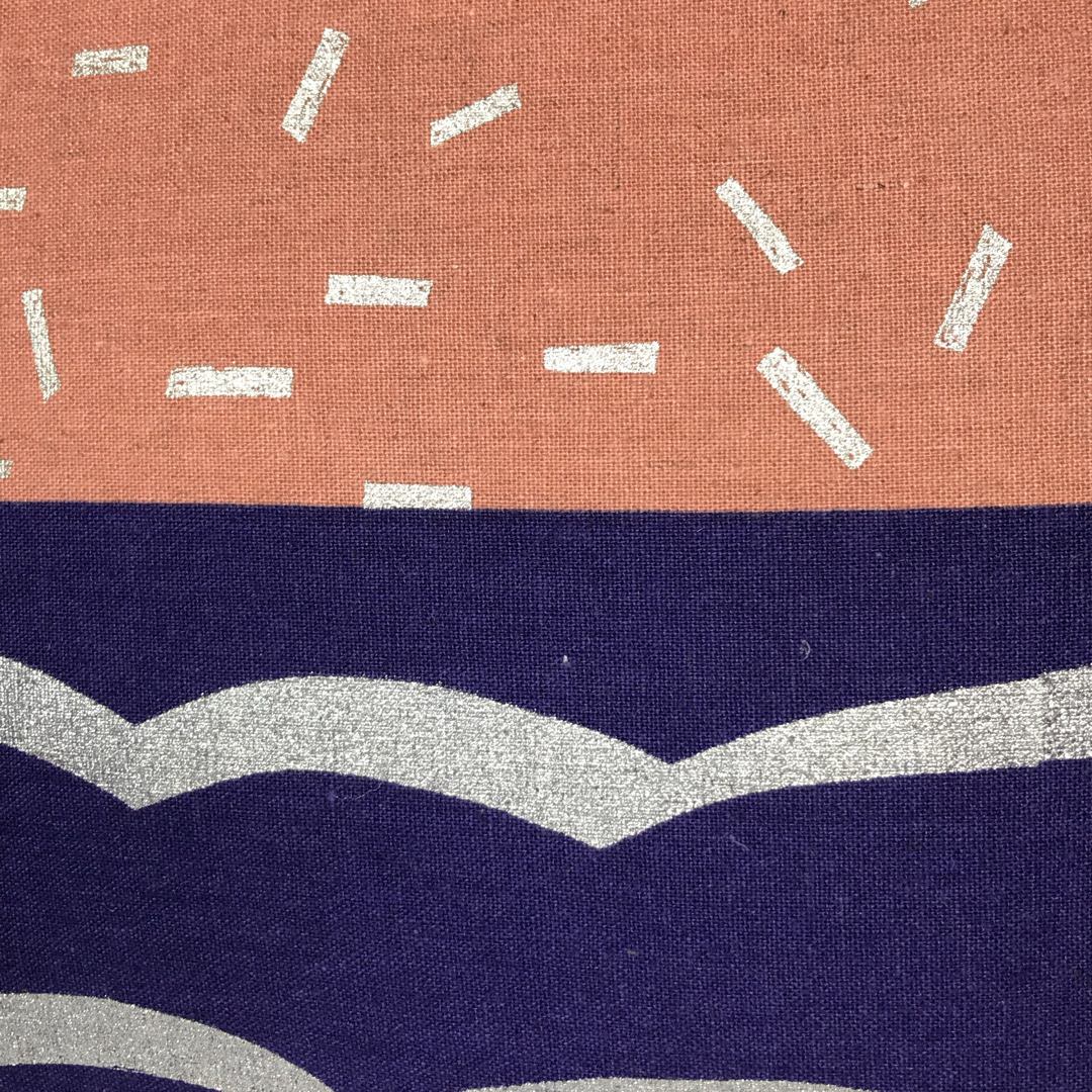 A cushion cover with a geometric design, featuring a purple and silver wave pattern on the bottom half and blush with silver speckles on the top half.