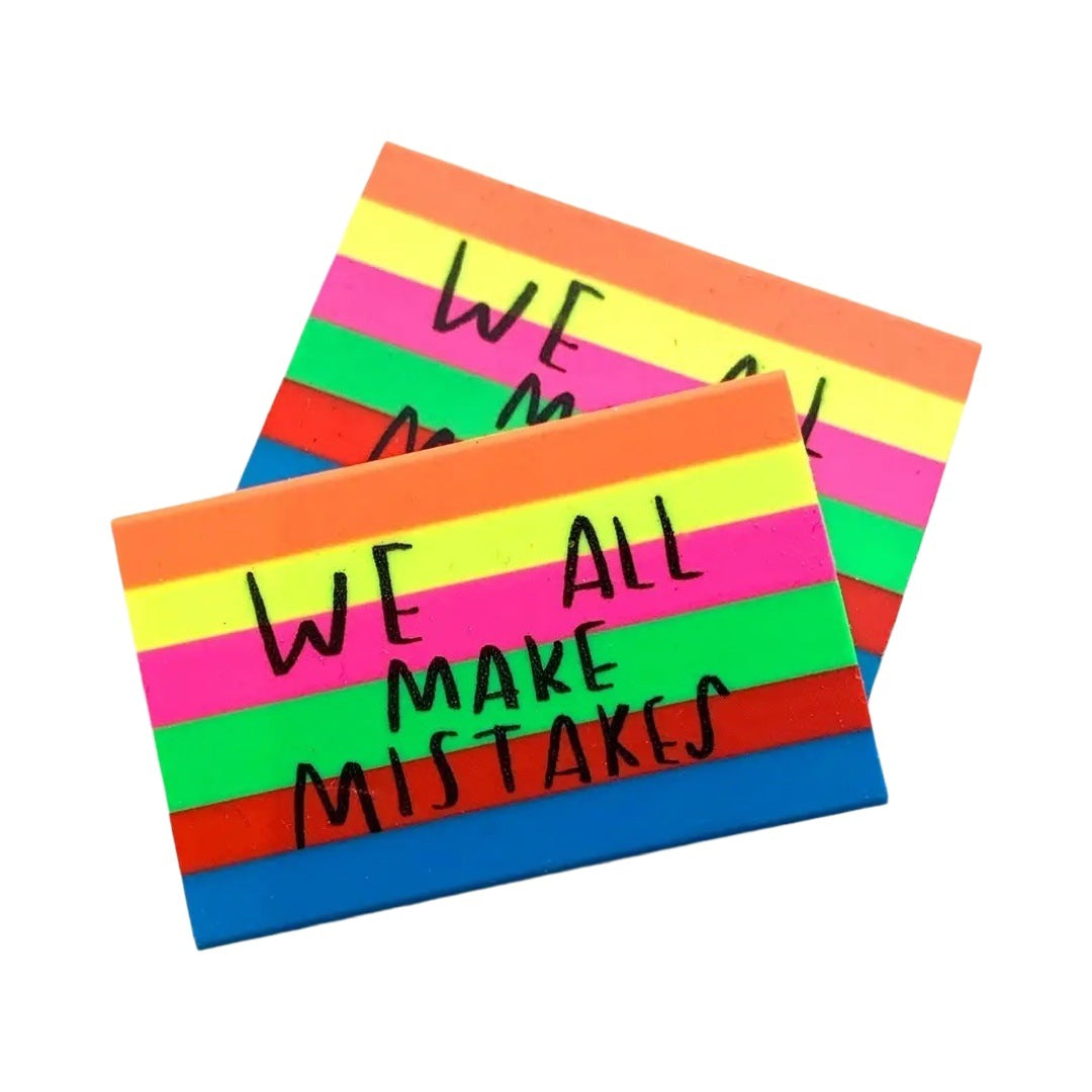 A colorful eraser with rectangular shape featuring rainbow stripes and the text 'We all make mistakes' in the center.