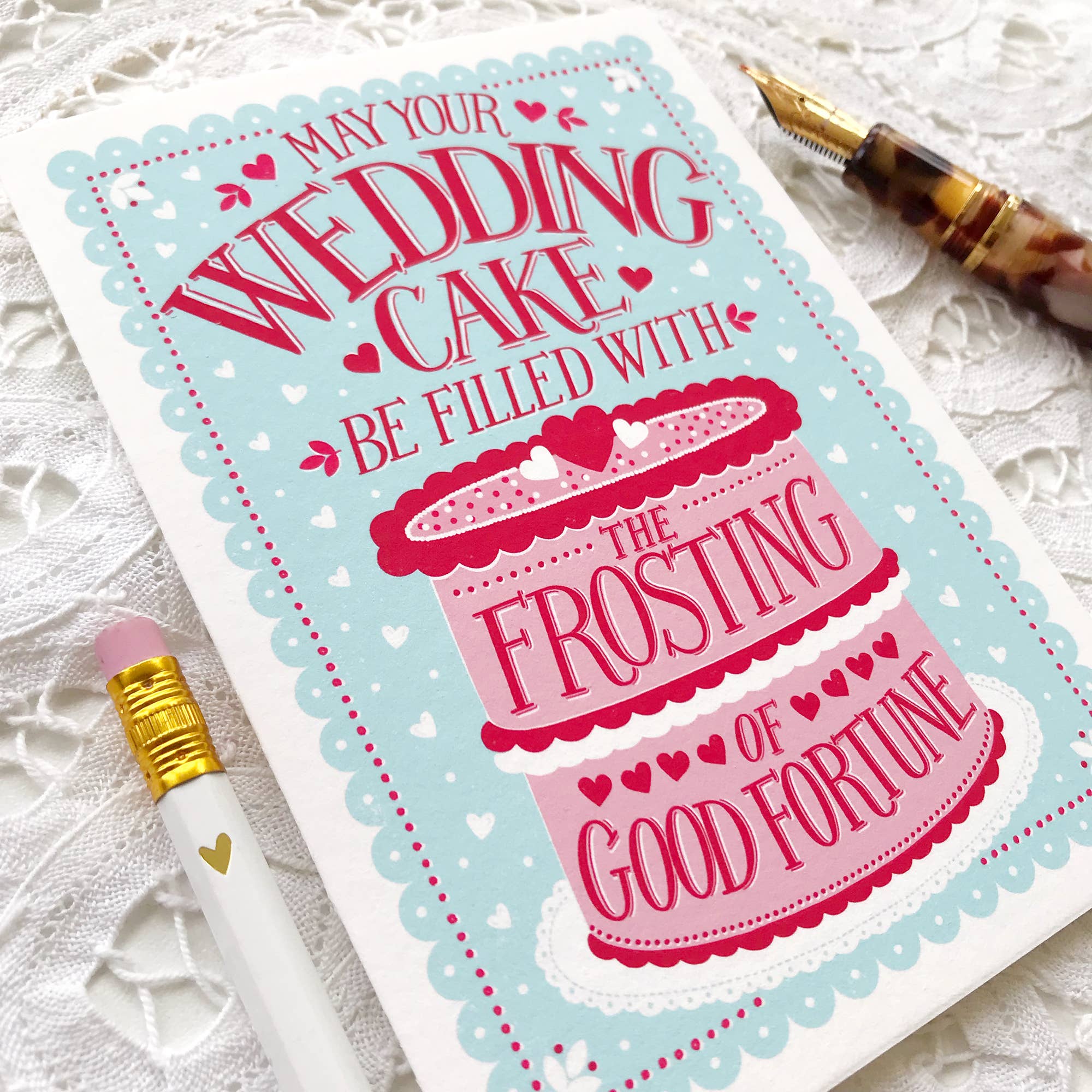 Card with wedding cake design and text on a textured surface with a pen.