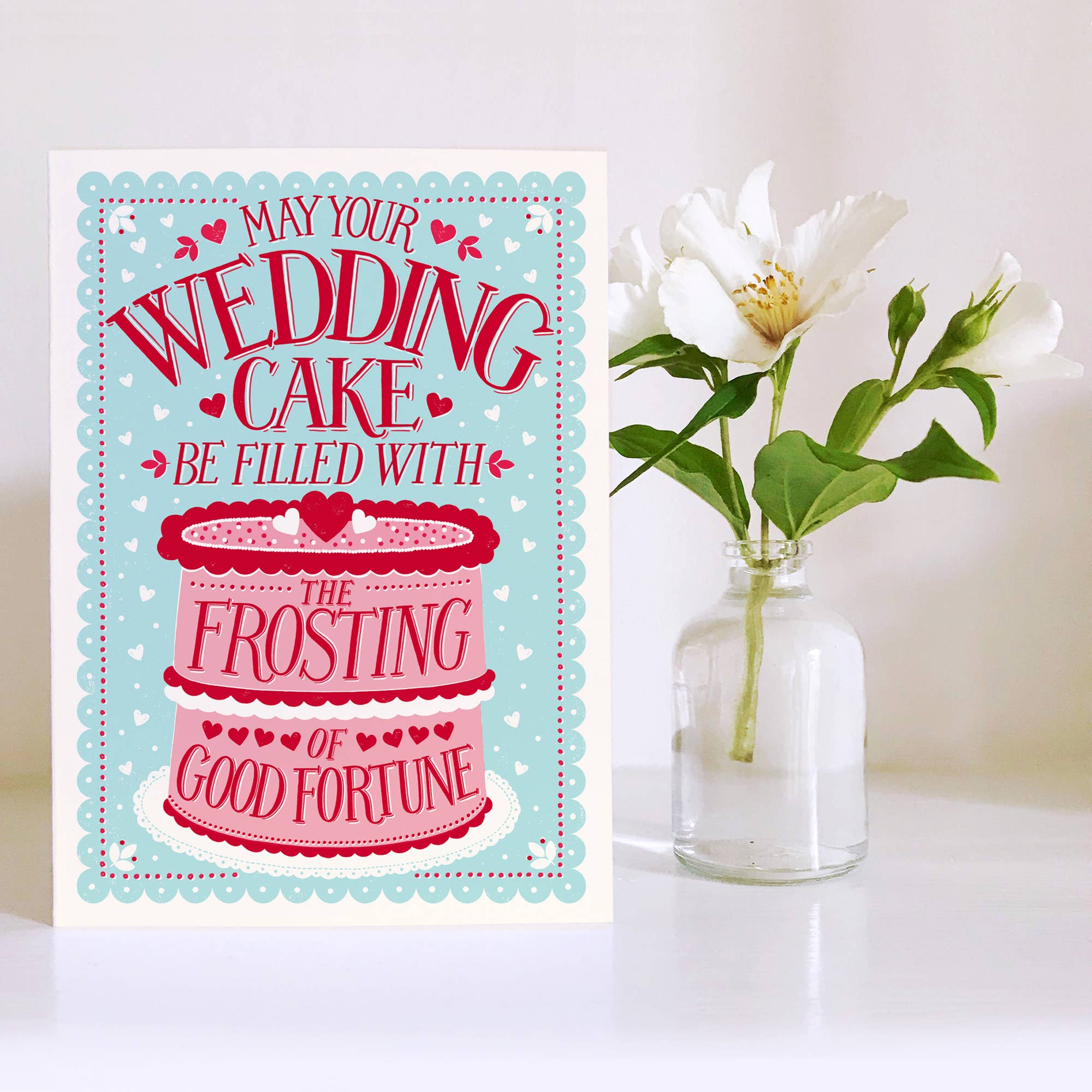 Wedding card with cake illustration and flowers in the background.