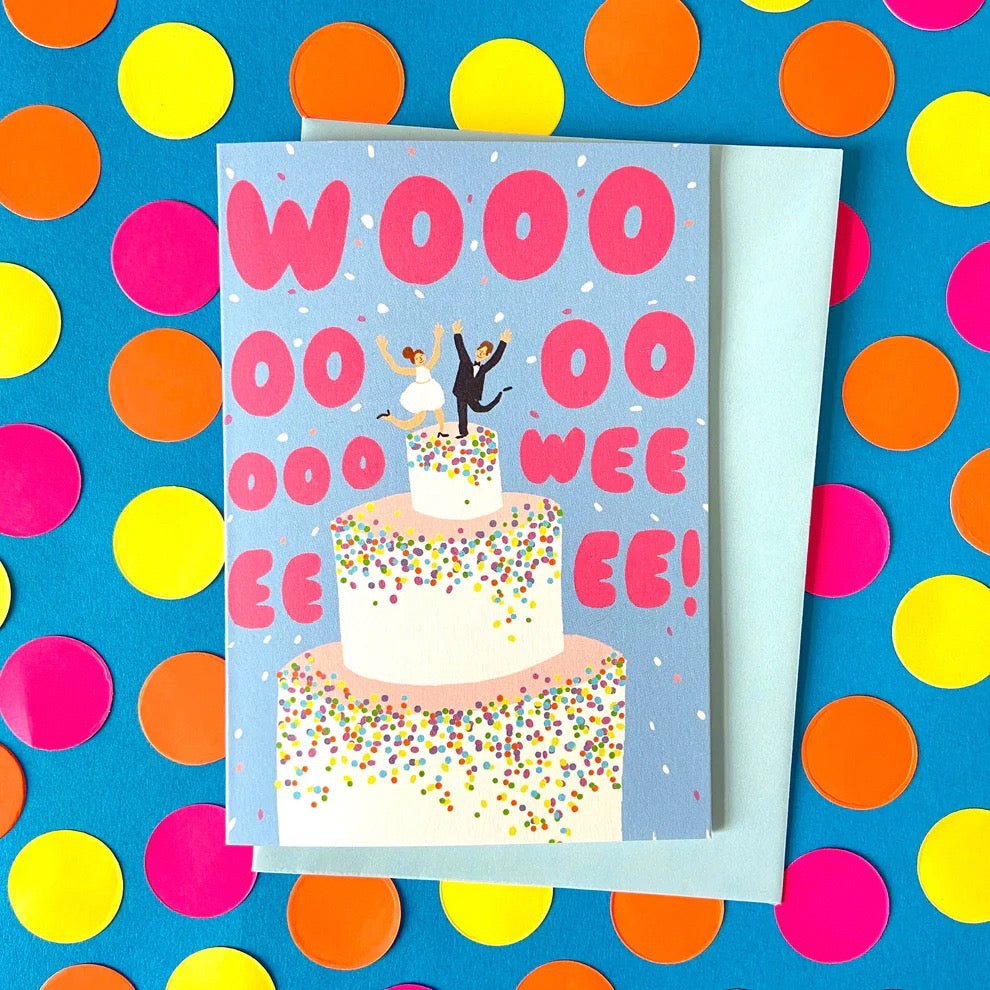 Card with a wedding couple on a cake, surrounded by 'OO WEE EE!' text and colourful confetti, on a polka dot background.