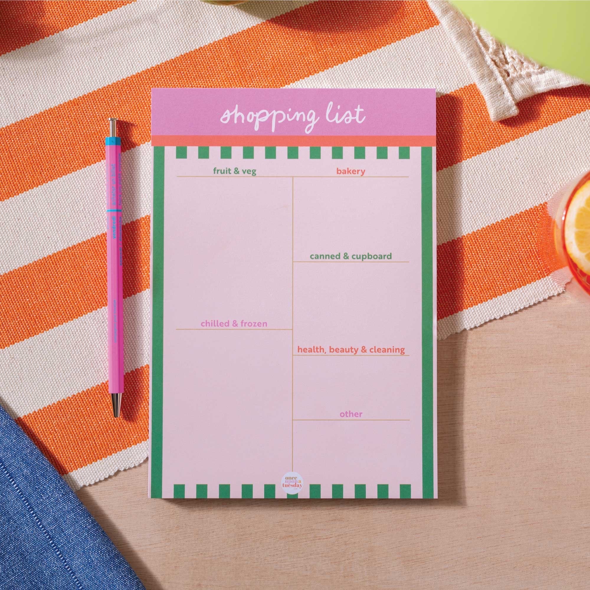 Notepad with a shopping list on an orange and white striped cloth.