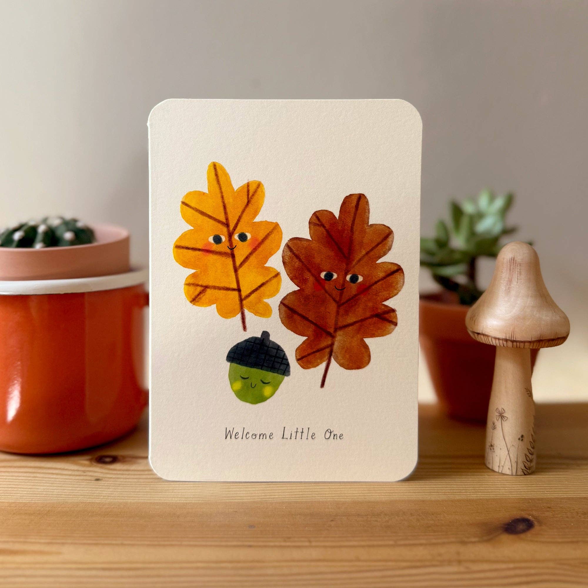 Greeting card with autumn-themed design featuring leaves and an acorn on a wooden surface.