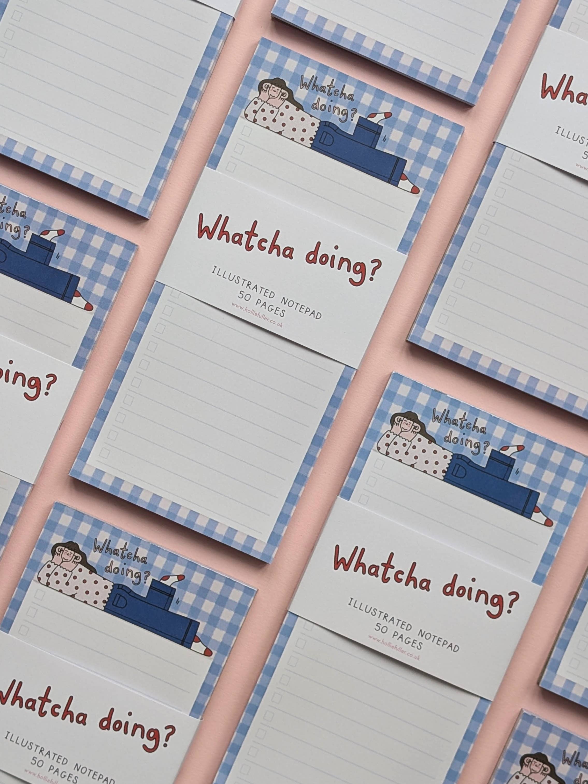 Stack of 'Whatcha doing?' illustrated notepads with a blue checkered border and a cartoon woman.