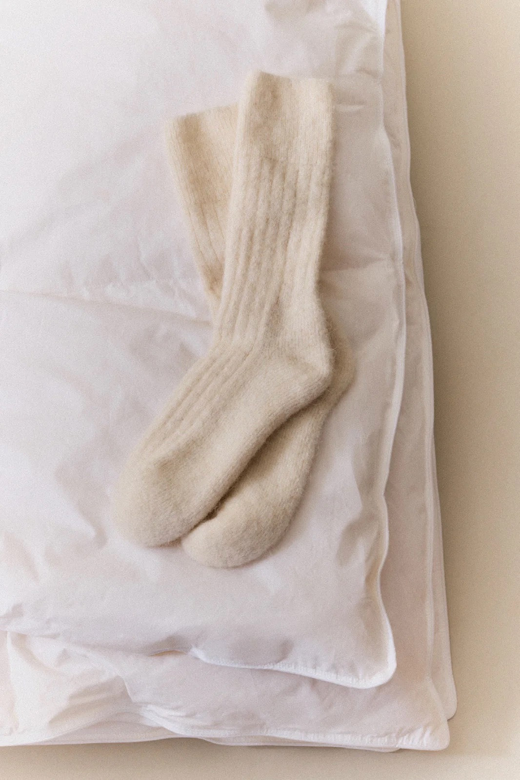 Pair of white fluffy socks on a white pillow.