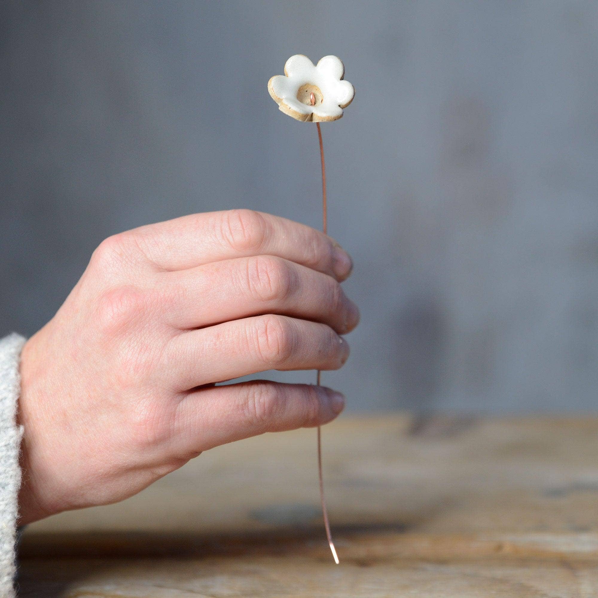 A hand holding a white ceramic flower bud stem on a copper wire