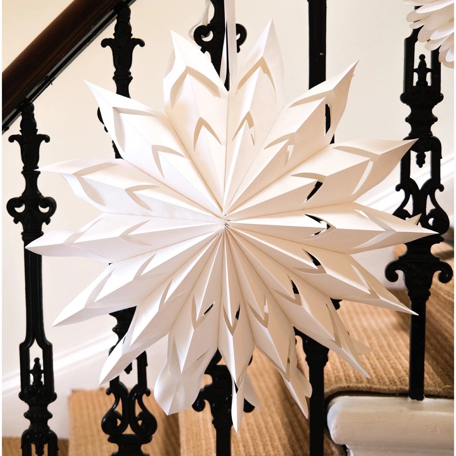 A fold out white paper star hanging n a black bannister.