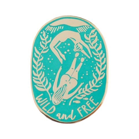 An oval-shaped turquoise enamel pin badge featuring two female wild swimmers and the text 'Wild and Free'.