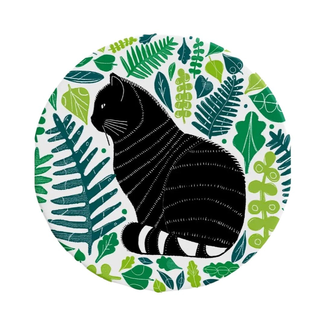 A round ceramic coaster featuring an illustration of a black wild cat surrounded by green leaves.