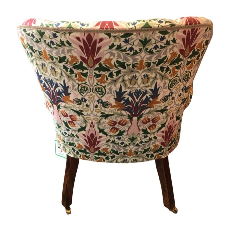 A hand-crafted occasional armchair in cream linen fabric with a multicoloured floral William Morris inspired design, featuring mahogany legs and gold castors.