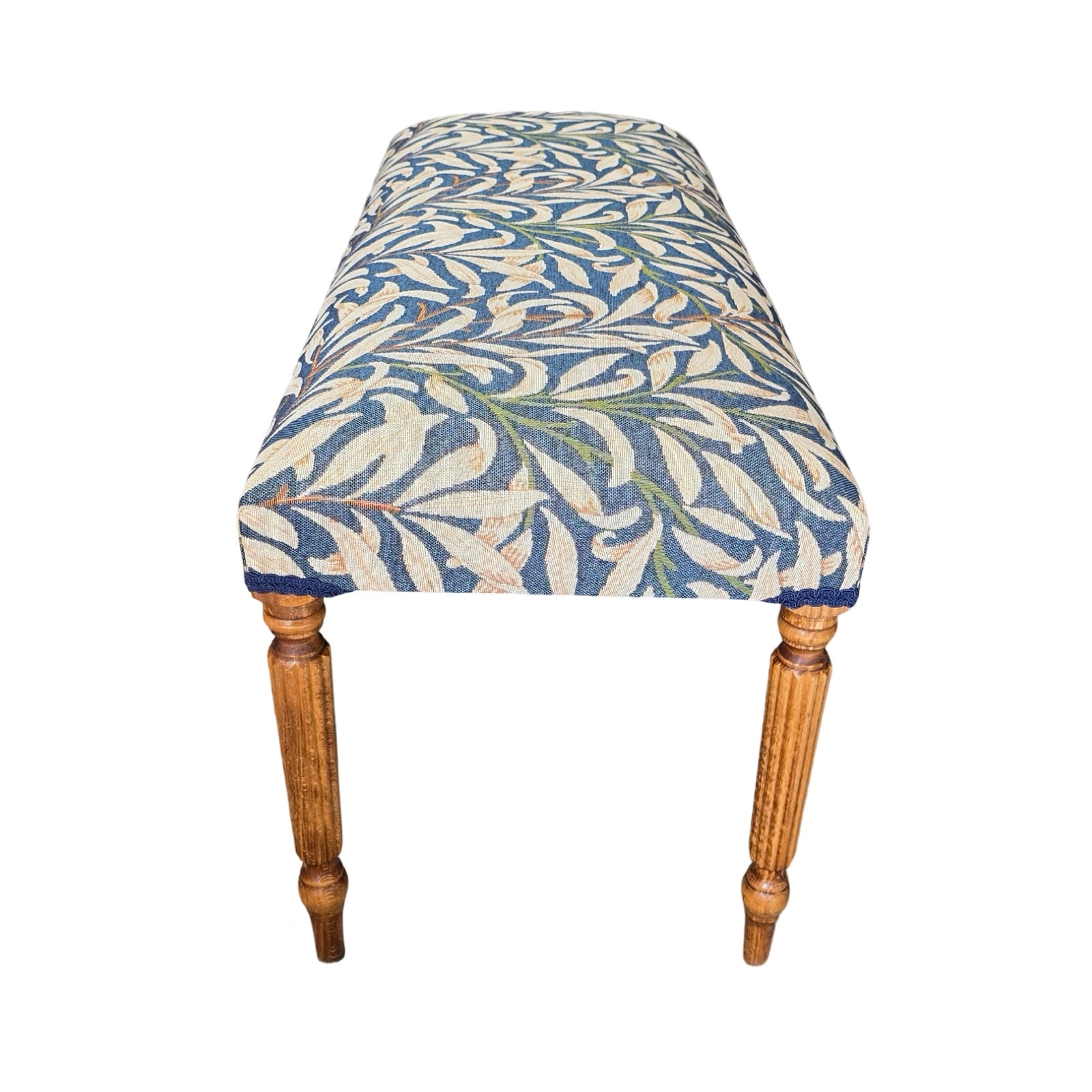 A rectangular bench covered in beautiful William Morris Willow Bough tapestry-style fabric in navy blue and cream. It is finished with navy blue binding and has mahogany-stained wooden legs.