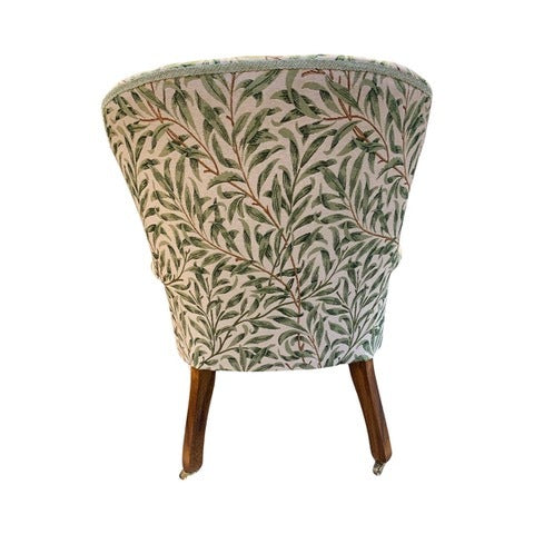 A William Morris style armchair with green leaf pattern on fabric, button-back design, and mahogany stained legs.