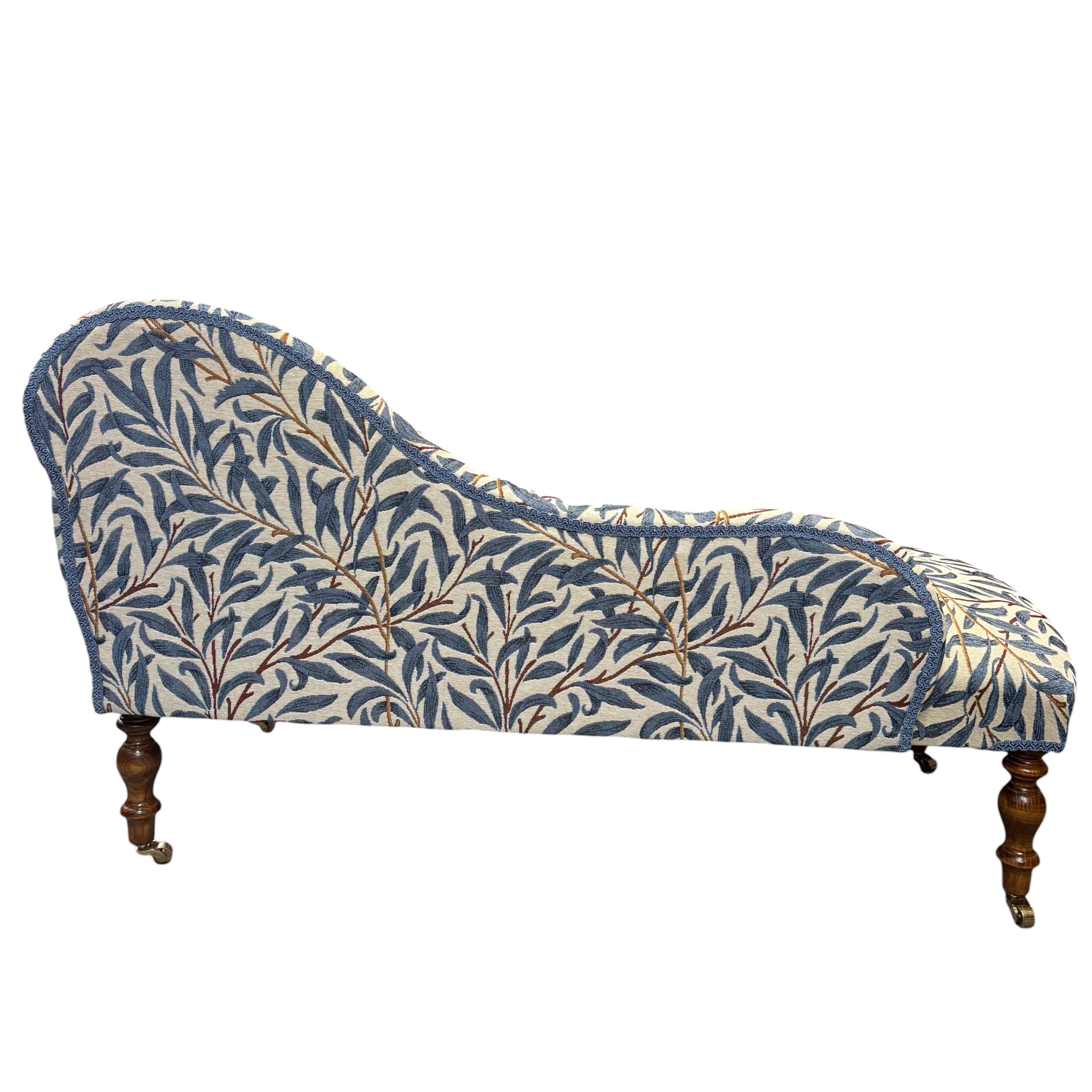 A handcrafted occasional chaise lounge in fabulous&nbsp;woven William Morris It is covered in beautiful William Morris Willow Bough tapestry-style fabric in navy blue and cream. It is finished with navy blue binding and has mahogany-stained wooden legs. The chaise lounge also comes with a removable bolster cushion and brass coloured castors.